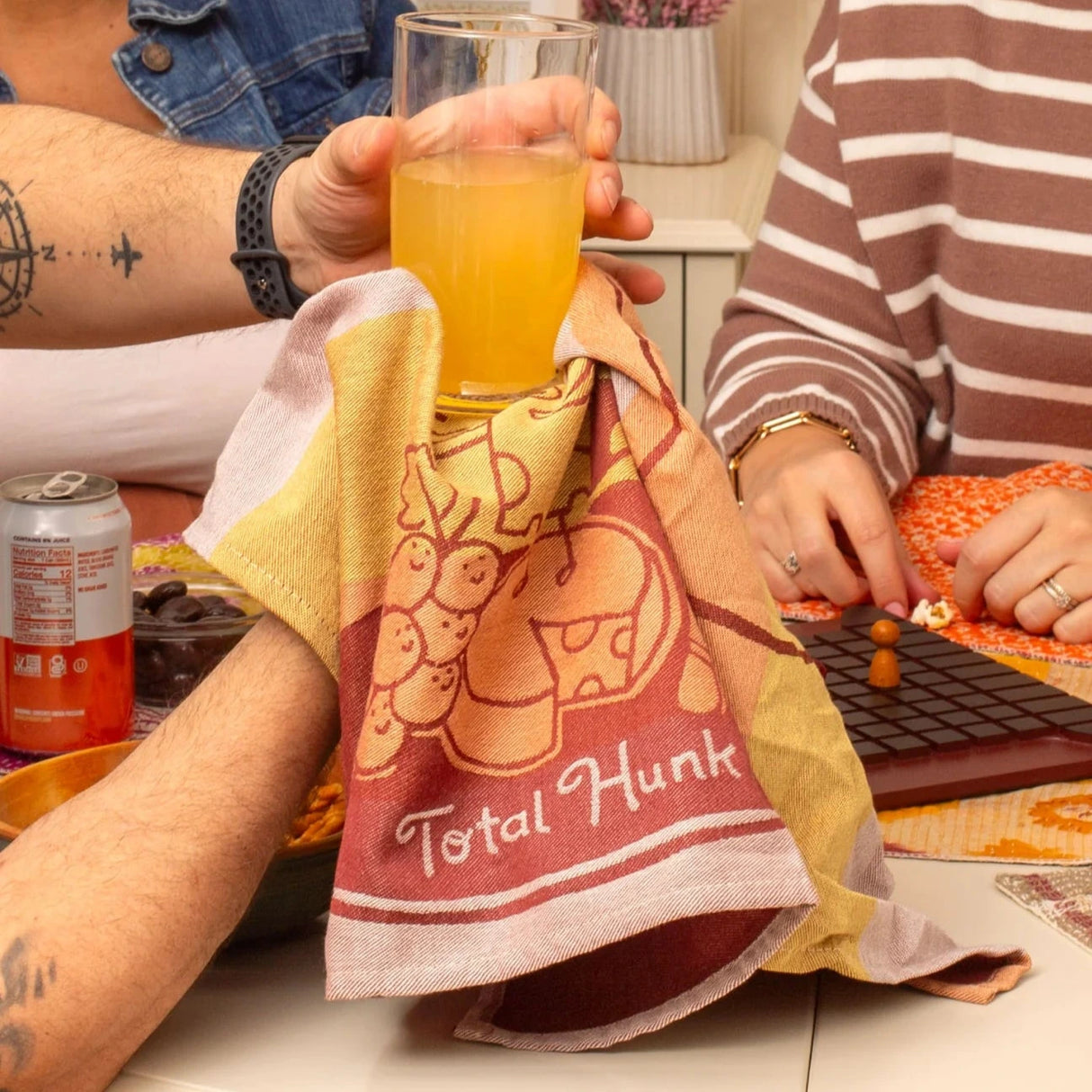 A group of people hold a glass with the dish towel. Reads, "total hunk." Photo © Blue Q