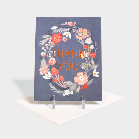 Greeting card with floral wreath imagery surrounding foil-stamped text.