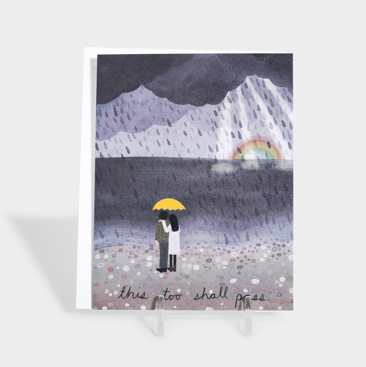 Greeting card with an illustration of a stormy beach. Two people stand under a yellow umbrella. A rainbow is seen beyond the clouds.